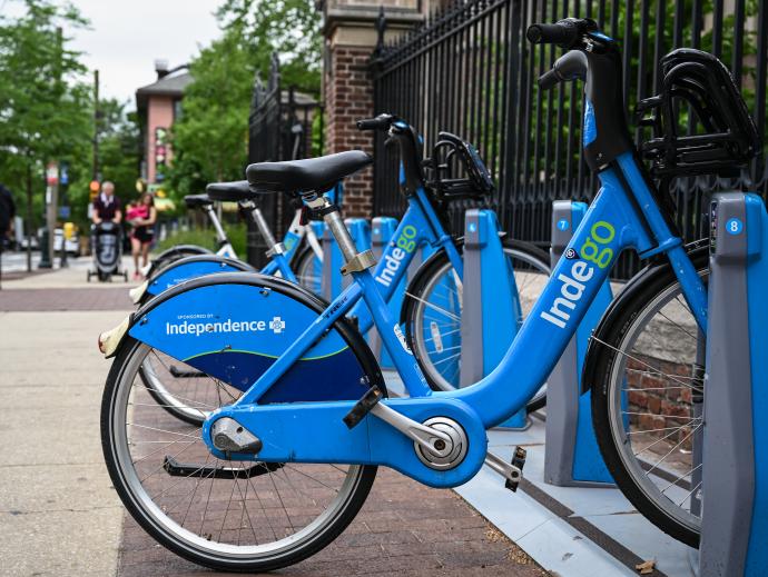 A bike share rack with several Indego bikes appear on a sidewalk near an iron gate