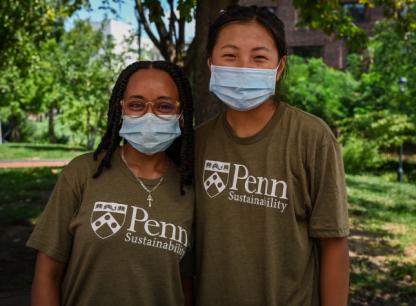 Two students wearing Penn shirts and masks posing under tree canopy